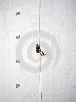 Worker hanging from rope on building wall
