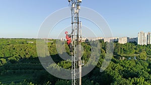 Worker in hard hat climbs high on radio telecommunication tower on background beautiful city landscape, aerial view of