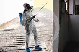 Worker in hazmat suit wearing face mask protection while making disinfection inside city building - Coronavirus decontamination photo
