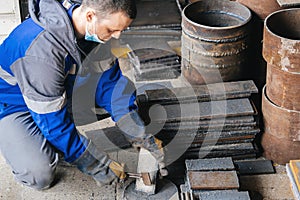 Worker in heavy industry or metallurgy beats scale off iron plates with hammer. Work with metal. Authentic workflow.