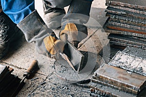 Worker in heavy industry or metallurgy beats scale off iron plates with hammer. Work with metal. Authentic workflow.