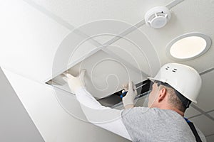 A worker in a helmet dismantles the suspended ceiling to test the lighting