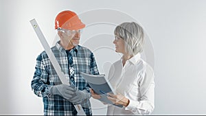 A worker in a helmet and a female engineer with a tablet and a level in their hands discuss plans for the reconstruction