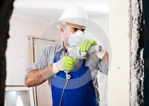 Worker in helmet is perforating wall with drill