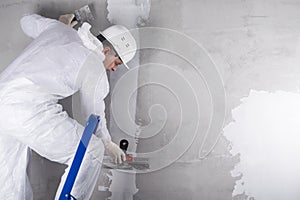 A worker in a helmet and a suit stands on a stepladder and applies the mixture to the wall to level it