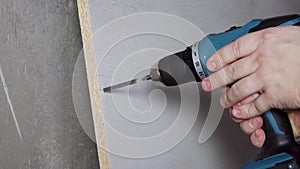 The worker with the help of a tool makes holes in the chipboard