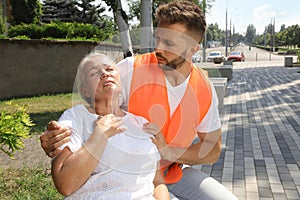 Worker helping mature woman on city street. Suffering from heat stroke