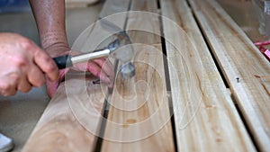 A worker is hitting a nail on a wooden board with a hammer