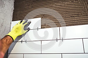 Worker holding ceramic tiles and applying cement adhesive on bathroom walls