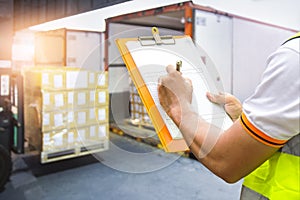 Worker Holding Clipboard is Control Loading Package Box into Cargo Container. Trucks Loading at Dock Warehouse. Shipment Delivery