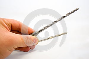 Worker holding in his hand 2 drills - one with carbide tip for rotary hammer, second - for usual drill. Illustration of choice dep