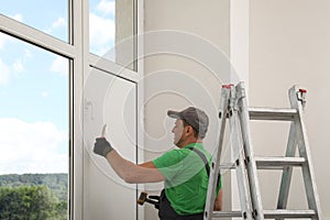 Worker holding knife and hammer indoors. Window installation