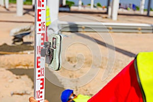 Worker is holding leveling rod to measuring level on construction site