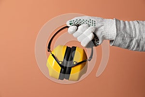 Worker holding safety headphones on coral background, closeup. Hearing protection device