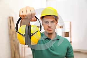Worker holding safety headphones indoors, focus on device. Hearing protection