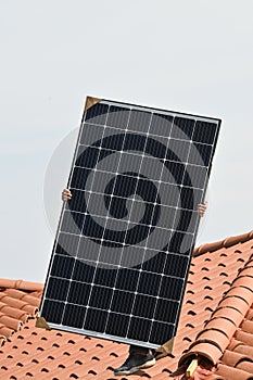 Worker holding solar panel on roof of residential house in construction