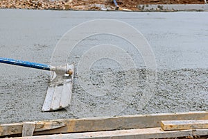 Worker is holding a steel trowel and smoothing plastering over freshly poured concrete that is wet