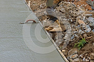 Worker is holding a steel trowel and smoothing plastering over freshly poured concrete that is wet