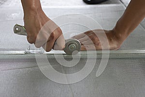 Worker holding a wheel tool to install a aluminum mosquito net wire mesh screen this is to be attached to the window of th