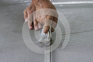 Worker holding a wheel tool to install a aluminum mosquito net wire mesh screen this is to be attached to the window of th