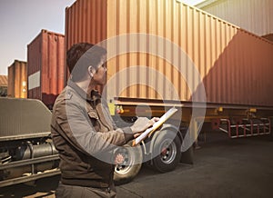 Worker Holds a Clipboard Controlling the Loading of Cargo into Shipping containers. Trucks Parked Loading at Dock Warehouse