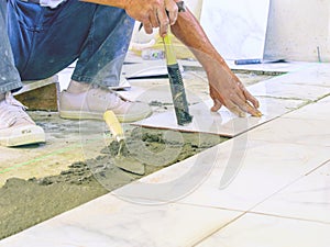 worker holds a hammer while laying tiles on the ground.