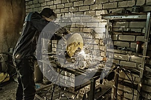 Worker holds hands the metall pipe to cut it on the machine. Against the background of white bricks