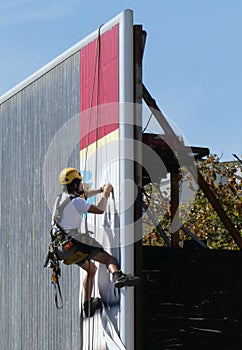 A worker hung on a rope changes an advertisement on a billboard