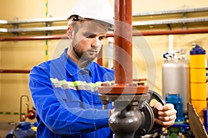 Worker on industrial plant. Technician operator turning gate valve on boiler system. Man in helmet and workwear services refinery