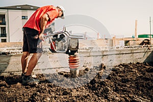 worker, industry details. Worker using vibratory compactor at house foundation