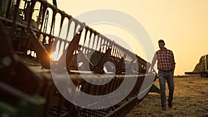 Worker inspect combine thresher countryside at golden sunset. Farming vehicle