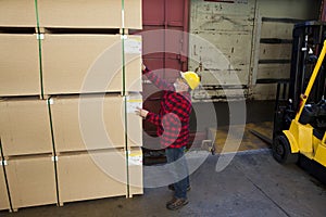 Worker inspecting wood pallet standing by fork lift truck