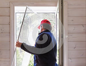 Worker install mosquito net or mosquito wire screen on wooden house window.