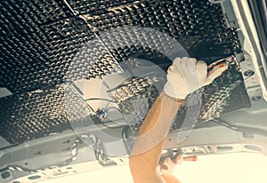 Worker installation soundproofing material to inside of car roof. Sound insulation for auto tuning