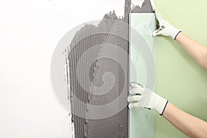Worker installing ceramic tile on wall, closeup