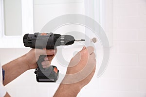Worker installing handle on cabinet door with screw gun in kitchen, closeup