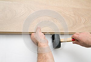 Worker installing laminate floor using a hammer