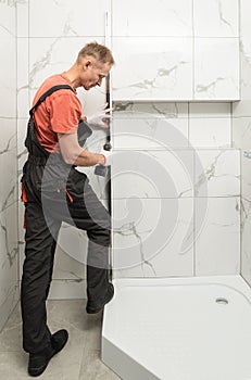 The worker is installing a metal profile of the shower cabin