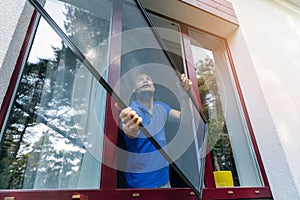 Worker installing mosquito net wire screen on plastic window