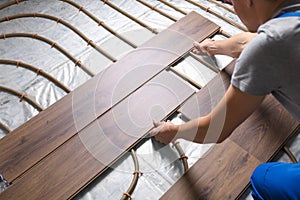 Worker installing new wooden laminate over underfloor heating system, closeup