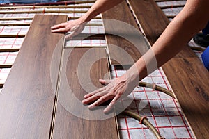 Worker installing new wooden laminate over underfloor heating system, closeup