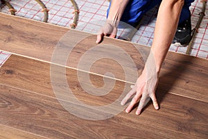 Worker installing new wooden laminate over underfloor heating system, closeup