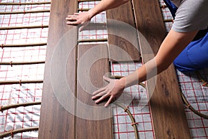 Worker installing new wooden laminate over underfloor heating system, closeup