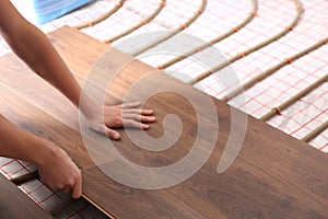 Worker installing new wooden laminate over underfloor heating system