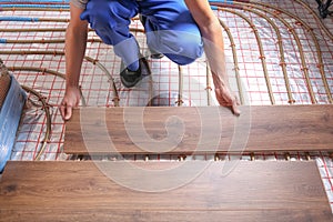 Worker installing new wooden laminate over underfloor heating system