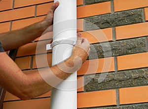 Worker installing rain gutter downspout pipe on the brick house. Guttering