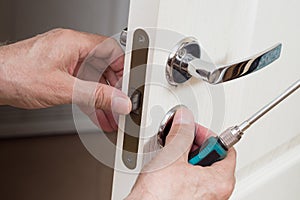 Worker installing or repairing new lock and door knob with screwdriver.