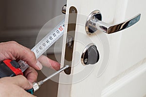 Worker installing or repairing new lock and door knob with screwdriver.