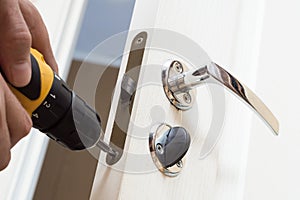 Worker installing or repairing new lock and door knob with screwdriver.