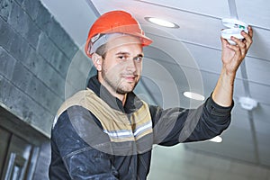 worker installing smoke detector on the ceiling. Fire alarm system installation